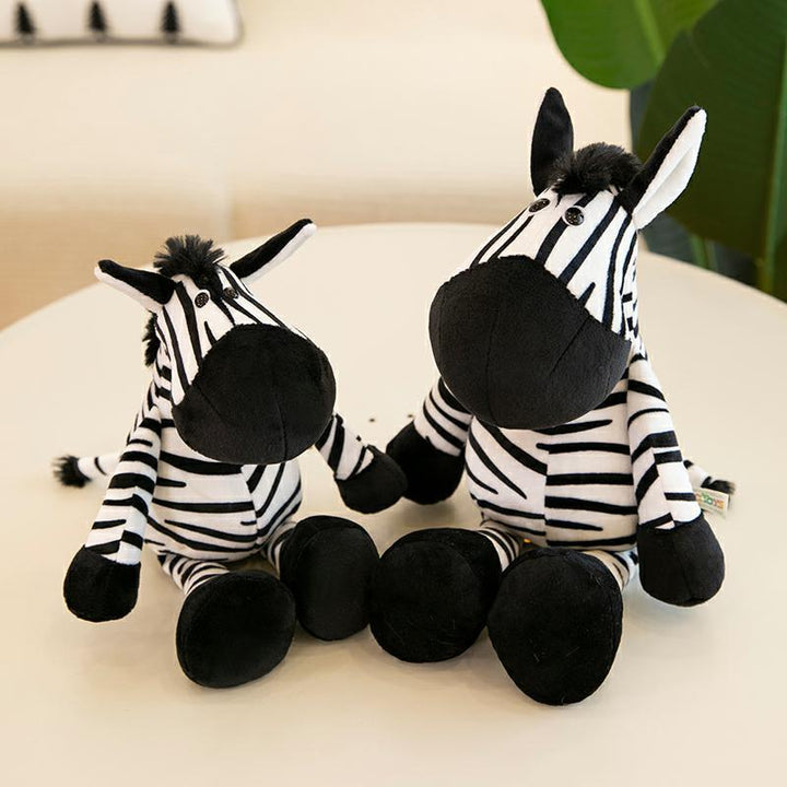 Two plush zebra toys sitting on a light surface with a blurred background.