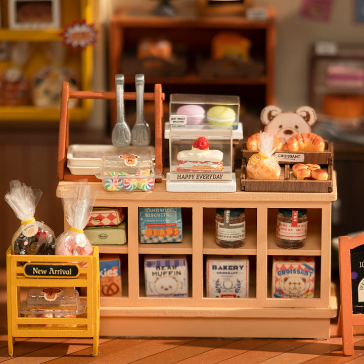 Miniature bakery display with various items on a wooden shelf.