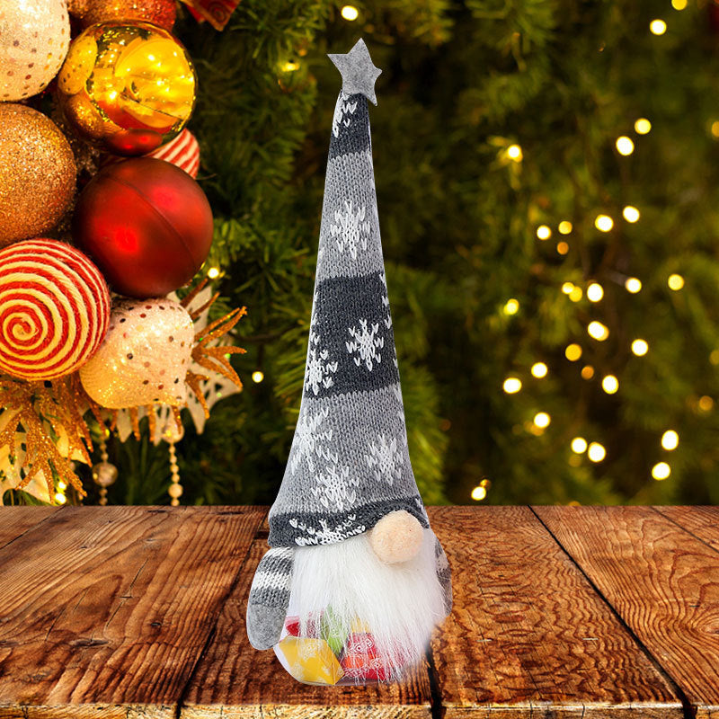 Decorative gnome with a striped hat on a wooden surface with Christmas ornaments and lights in the background.
