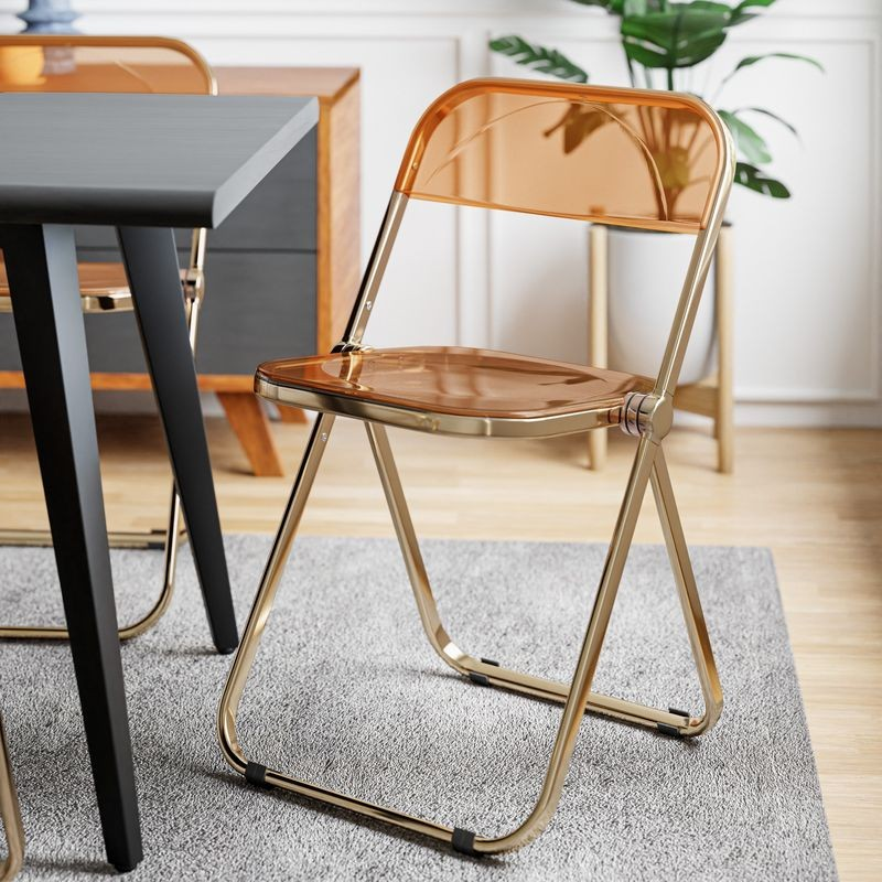 LeisureMod Lawrence Acrylic Folding Chair with Gold Metal Frame Tangerine at Table.