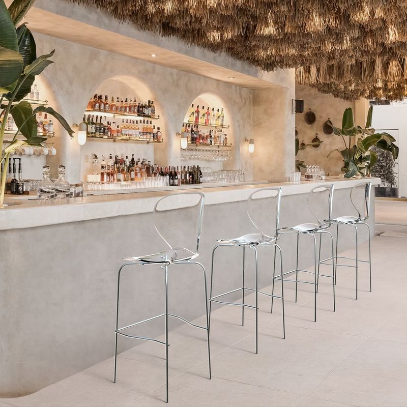 LeisureMod Oyster Acrylic Barstool with Steel Frame in Chrome Finish in Clear at Bar.