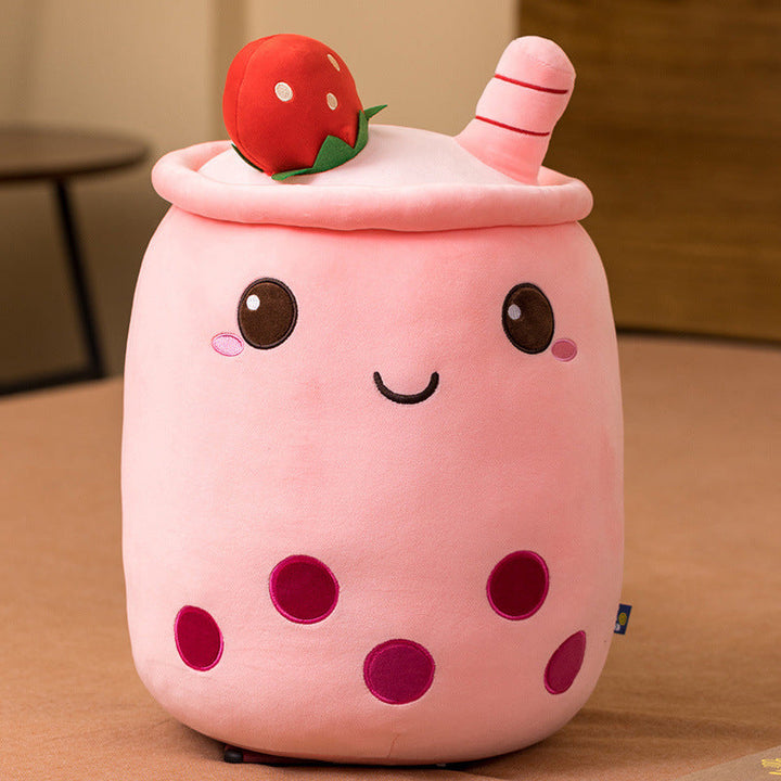 Pink plush toy resembling a bubble tea with a cherry on top on a wooden surface.