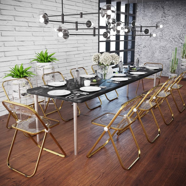 LeisureMod Lawrence Acrylic Folding Chair with Gold Metal Frame Transparent Black at the Table.