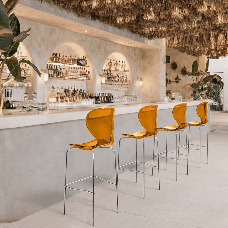 LeisureMod Oyster Acrylic Barstool with Steel Frame in Chrome Finish in Transparent Orange at Bar.
