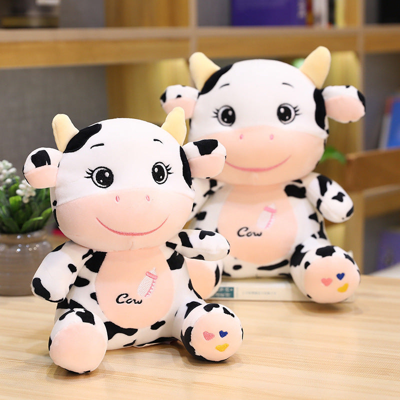 Two plush cow toys on a wooden surface with a blurred indoor background.