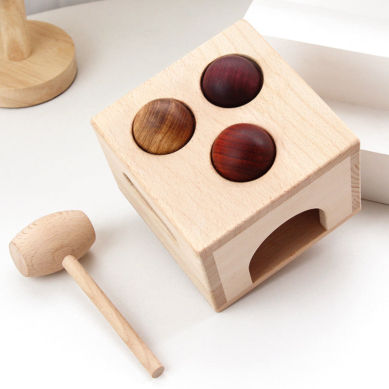 Wooden block puzzle with three colored spheres and a wooden hammer on a white surface.