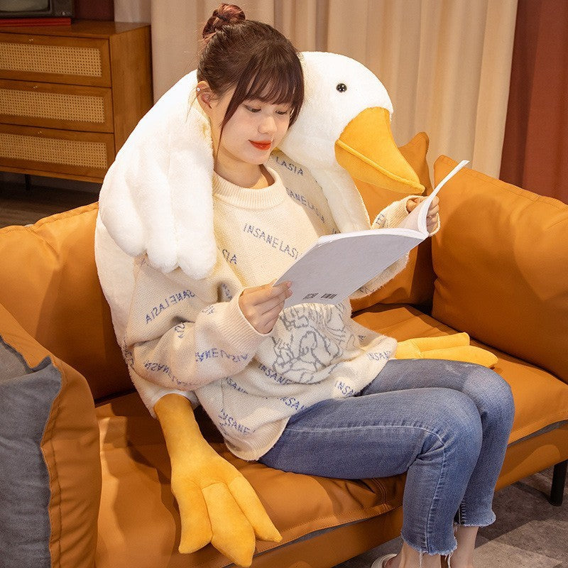 Person sitting on a couch with a large duck-shaped pillow reading a book.