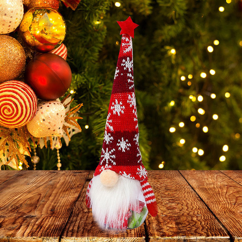 Decorative gnome with a red and white striped hat on a wooden surface with Christmas ornaments and lights in the background.