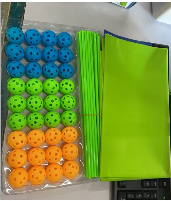 Packaged blue, green, and orange balls with green sticks and a green folder on a desk.