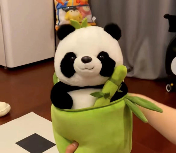 Plush panda toy in a green sleeve held by a hand on a wooden floor.