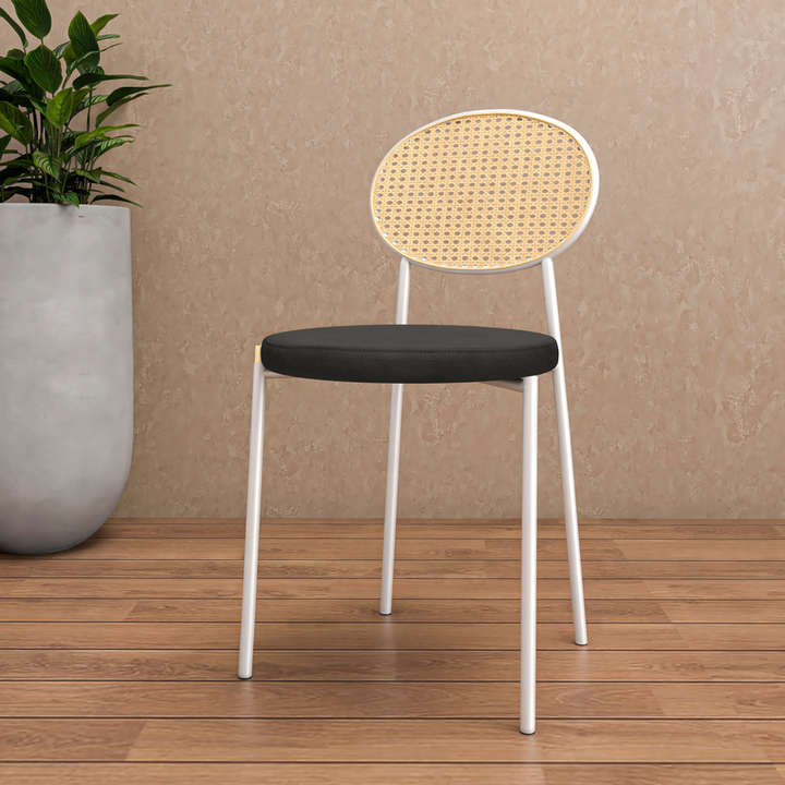 Chair with black seat and woven backrest on a wooden floor with a plant in the background.