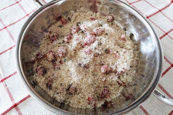 Metal strainer with berries and sugar on a red and white checkered tablecloth.