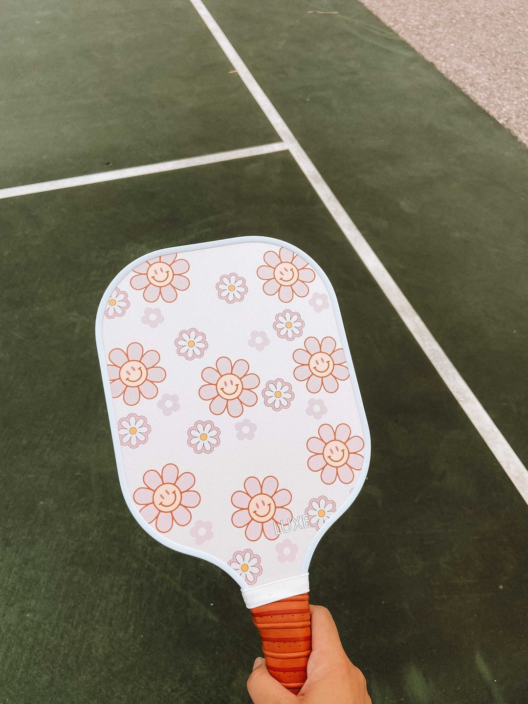 Pickleball paddle with floral pattern held on a green court.