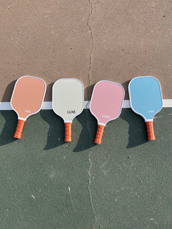 Four colorful pickleball paddles on a textured surface.