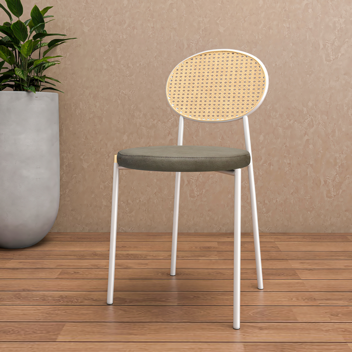 Chair with wicker backrest and green seat on a wooden floor with a plant in the background.