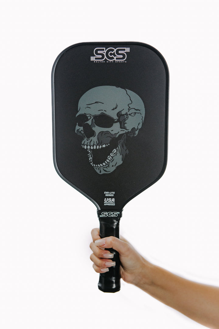 Pickleball paddle with skull design held by a hand on a white background.