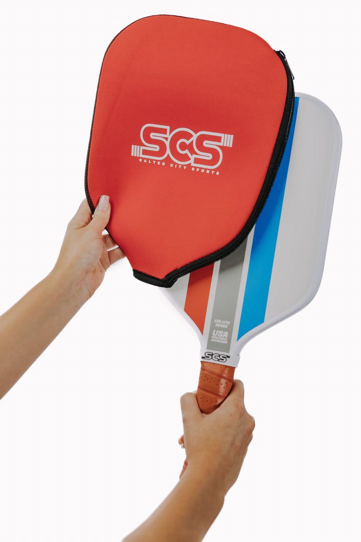 Red pickleball paddle with SCS branding held by a person on a white background.