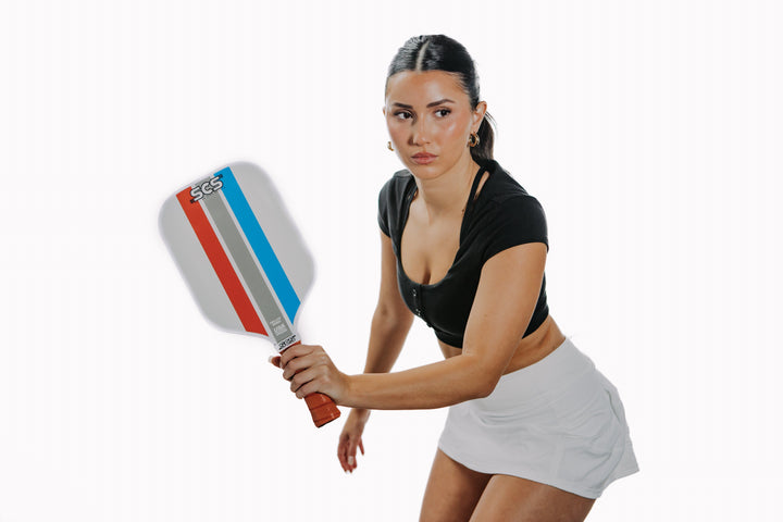 Woman holding a pickleball paddle with a white background.