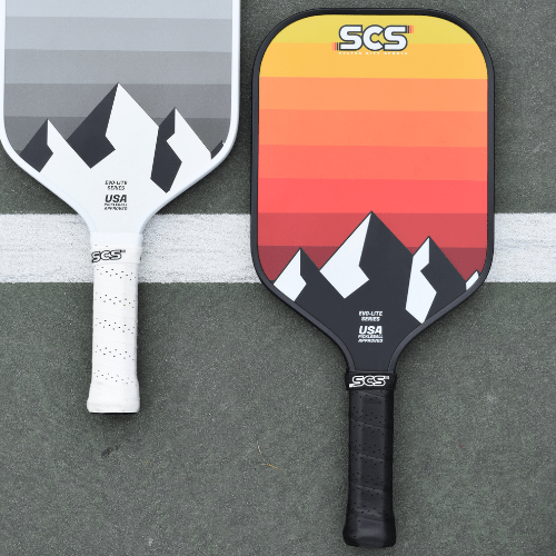 Two pickleball paddles with mountain design and branding on a gray surface.