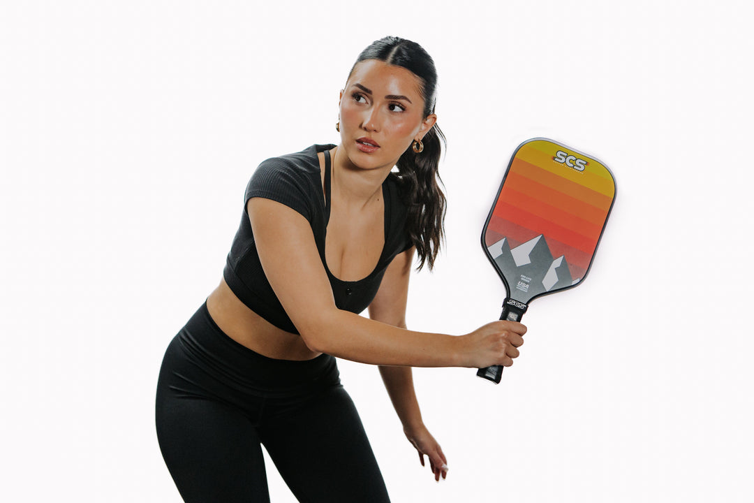 Woman holding a pickleball paddle with a white background.