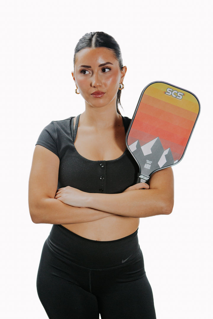 Woman holding a pickleball paddle with 'SCS' branding on a white background.