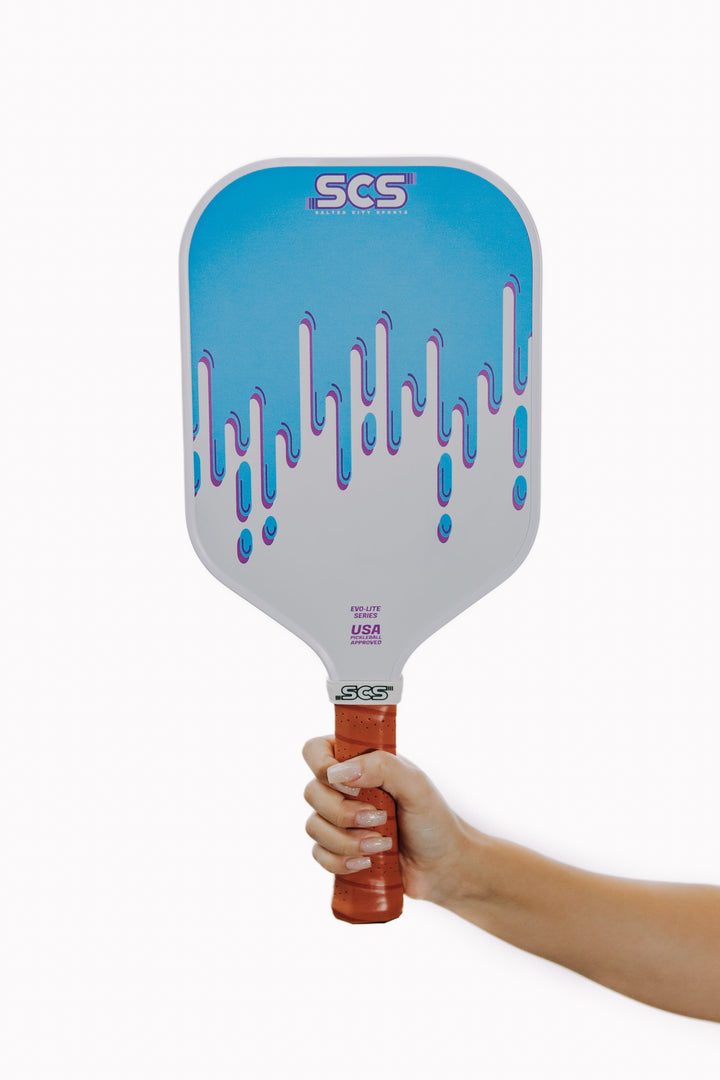 Blue and white pickleball paddle with 'SCS' branding held by a hand on a white background.
