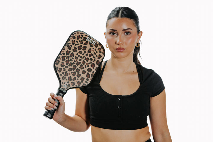 Woman holding a leopard print pickleball paddle against a white background.