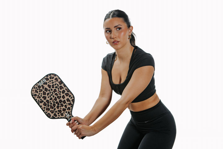 Woman holding a leopard print pickleball paddle on a white background.