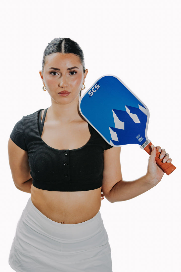 Woman holding a blue pickleball paddle on a white background.