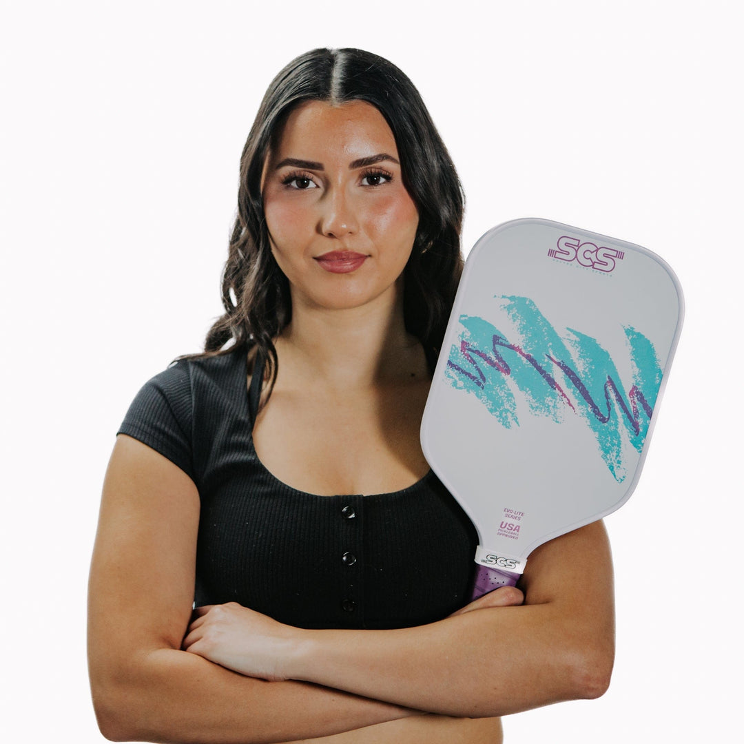 Woman holding a pickleball paddle with a white background.