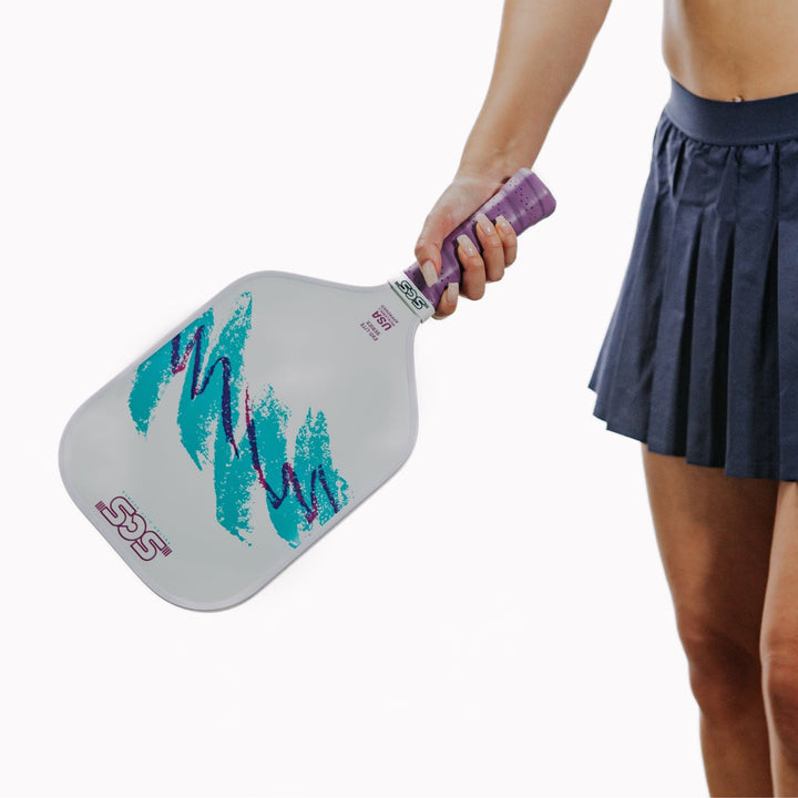 Person holding a pickleball paddle with a white background.