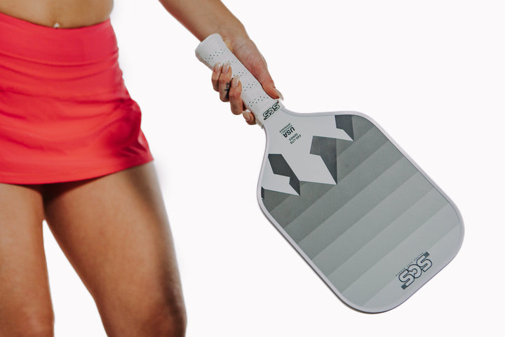 Person holding a gray pickleball paddle with a white handle on a white background.