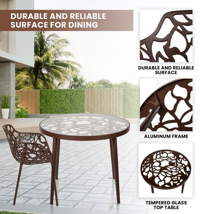 Outdoor dining table with decorative metal frame and tempered glass top, set against a garden backdrop.