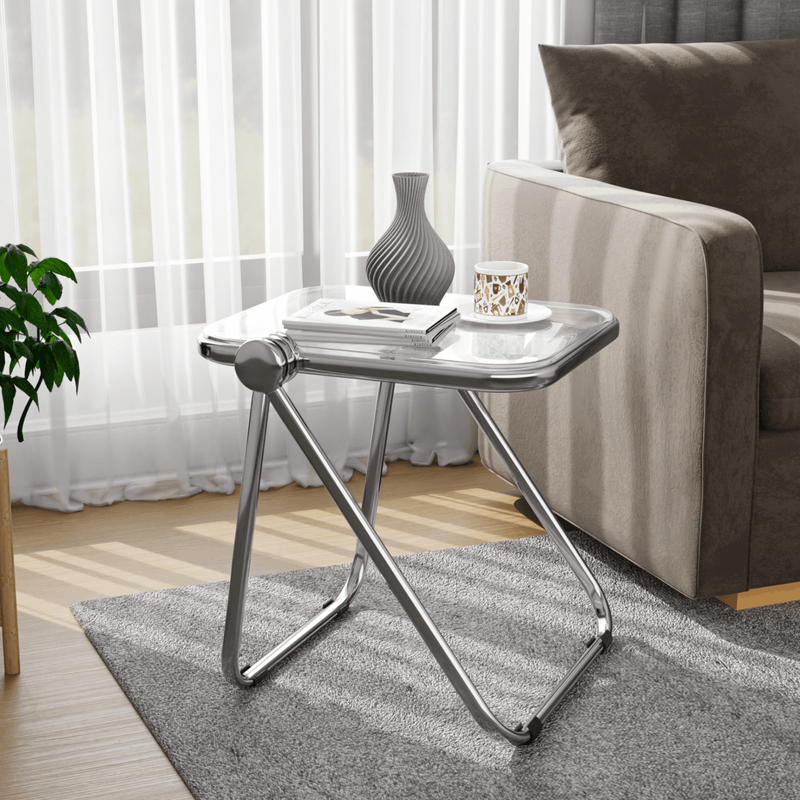 LeisureMod Lawrence Mid-Century Modern Rectangular Folding Side Table in Chrome Finish with Plastic Tabletop and Aluminum Frame Clear by Couch.